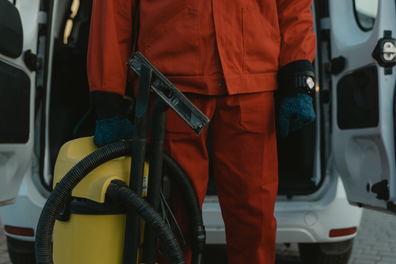 why-choose-us A professional cleaner in a red uniform holding a vacuum near a van, ready for service.