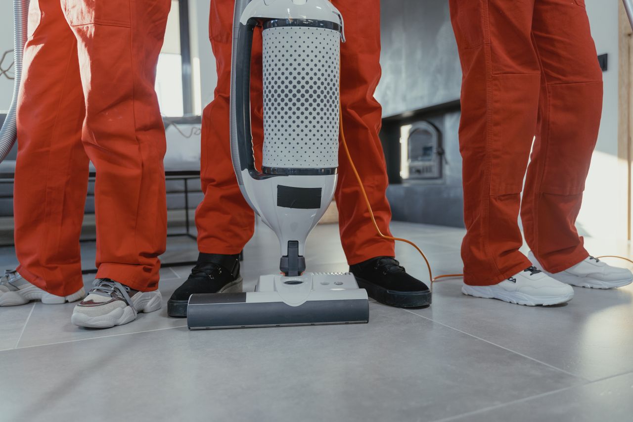 hero-img-01 Team of professional cleaners in red uniforms using a vacuum cleaner indoors.